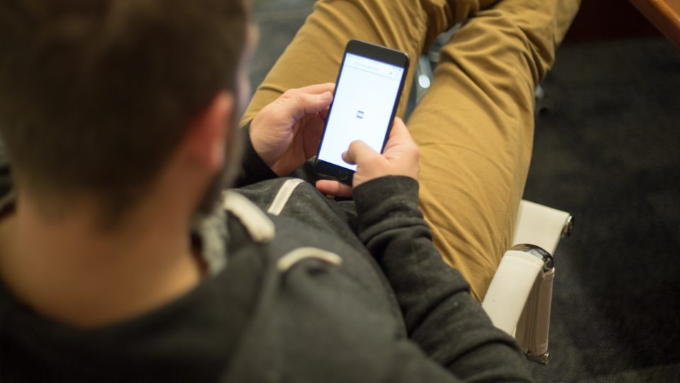 A person holding a smartphone, seen over the shoulder in natural light