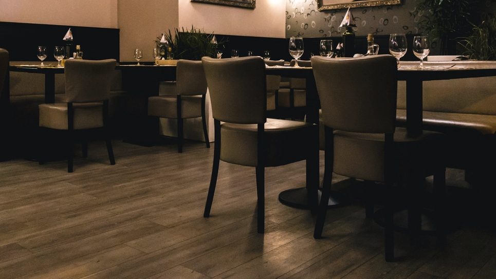 An empty restaurant dining room with dark wood tables laid for service
