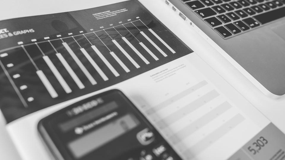 A printed bar chart on a desk beside a laptop, shot in black and white