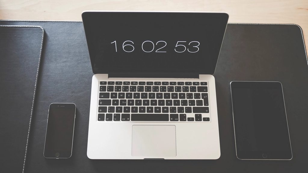 A laptop, a phone and a tablet arranged on a dark desk